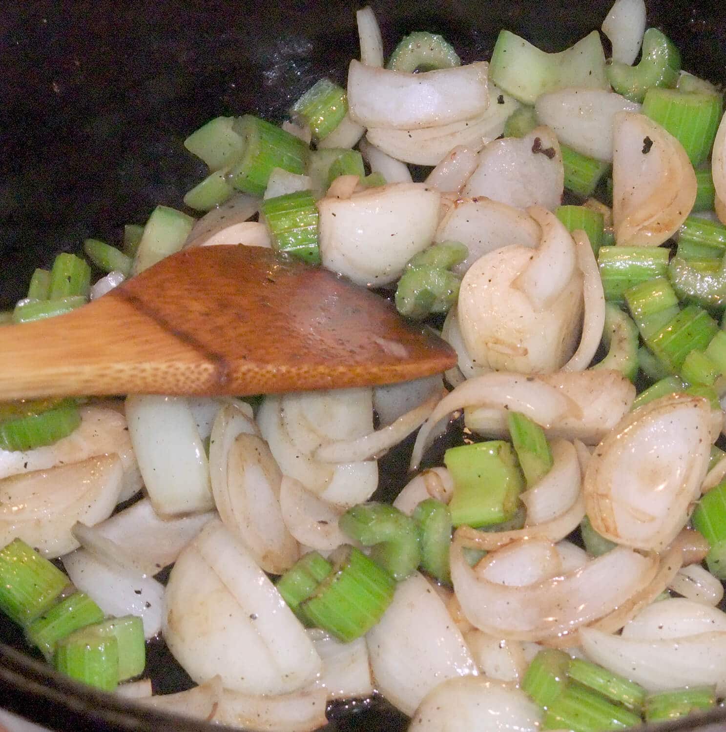 A wooden spoon stirring celery and onions in a large pot to make the best pot roast.
