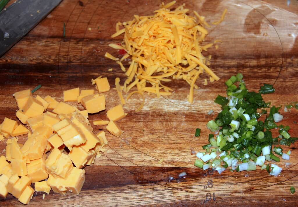 Cheese and green onions on a wooden cutting board.