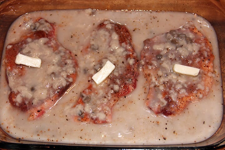 Pork chops in a glass baking dish with butter on top.
