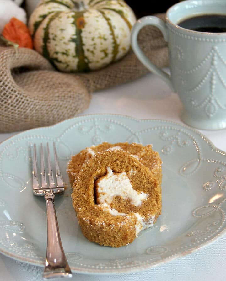 A slice of pumpkin roll on a plate with a fork.