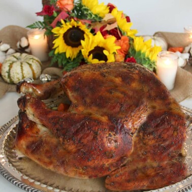 Roasted turkey on a platter with flowers in the background for Thanksgiving dinner menu.