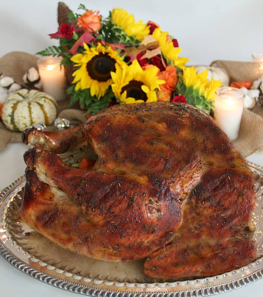 Roasted turkey on a platter with flowers in the background for Thanksgiving dinner menu. 