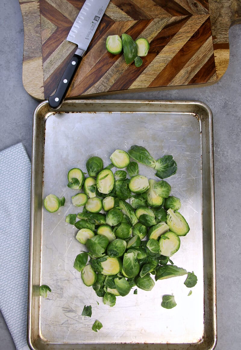 A baking sheet and cutting board with chopped Brussels Sprouts. 