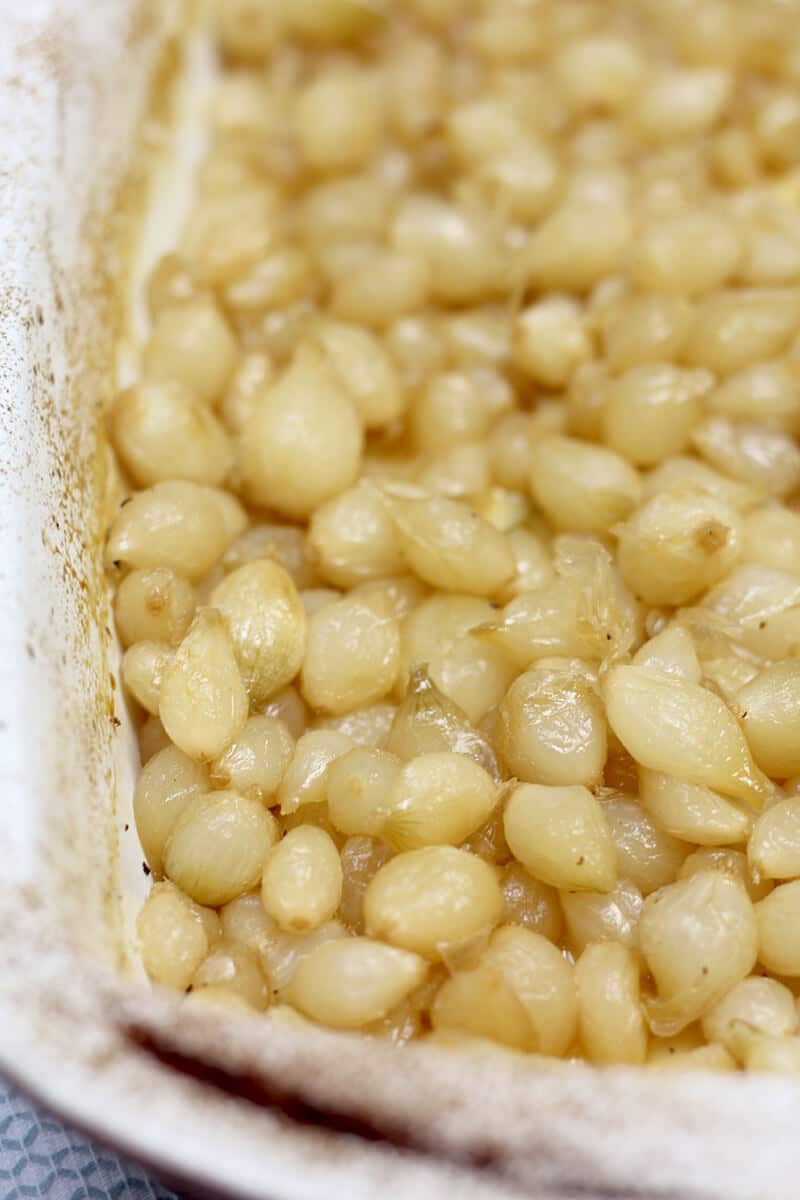 Closeup shot of roasted pearl onions in a baking dish.