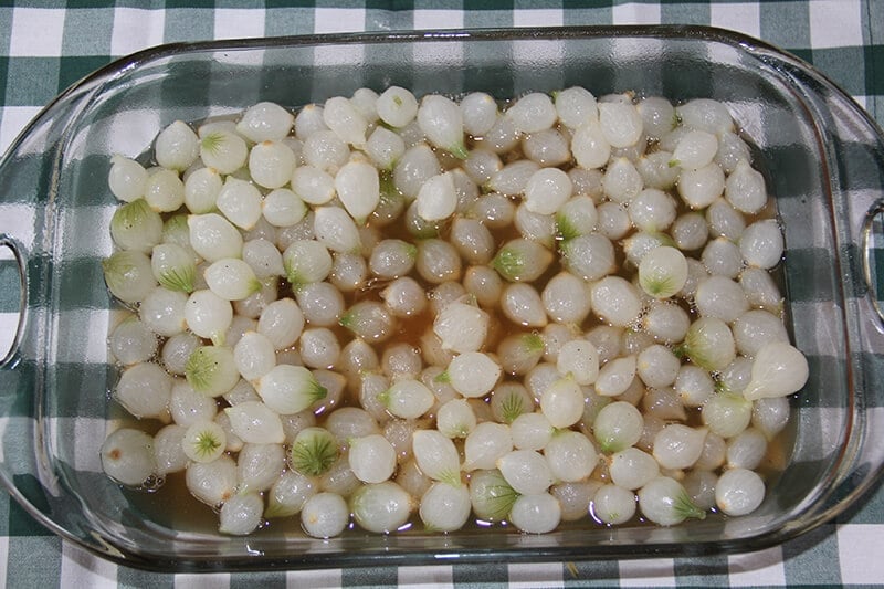 A baking dish with pearl onions crowded together. 
