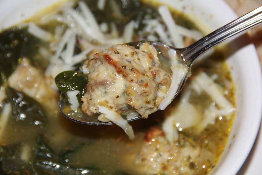 A spoonful of finished Italian Wedding Soup with a chicken meatball in the spoon.