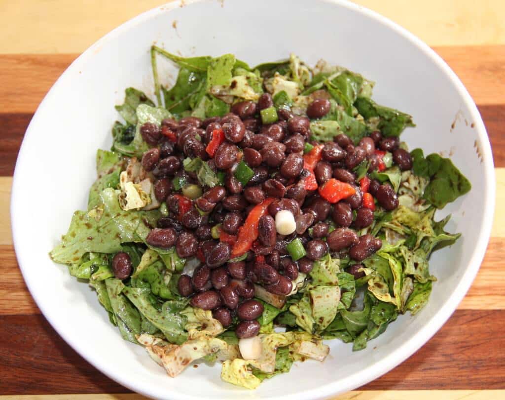 black bean salad on a bowl of greens in a white bowl