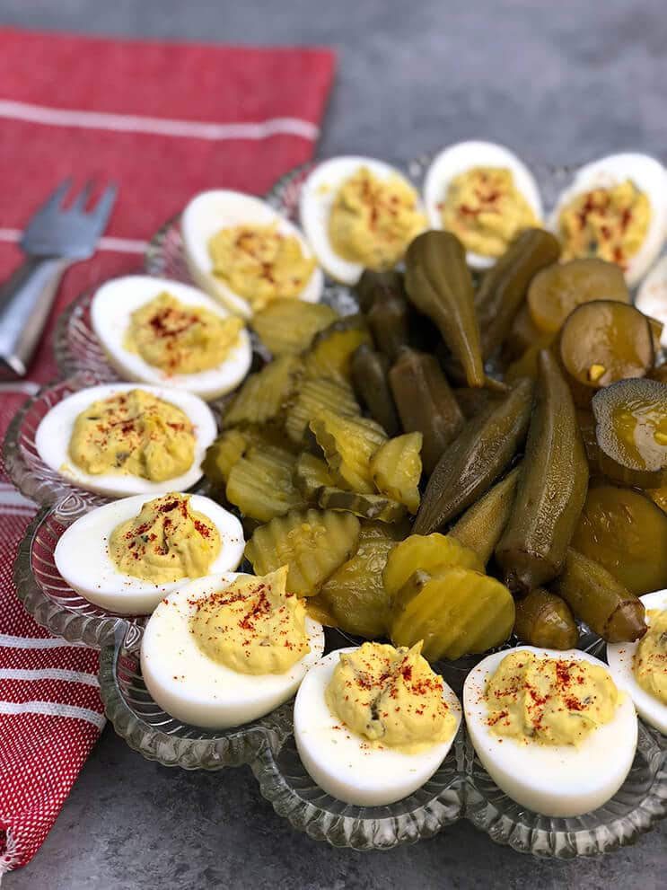 A platter of Southern deviled eggs with pickles on a red towel.
