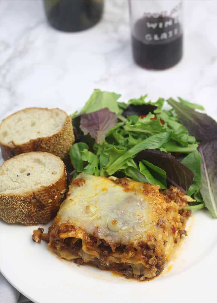 Serving of lasagna on a plate with salad and bread.