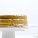 Side of a whole caramel cake on a white cake stand.