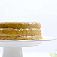 Side of a whole caramel cake on a white cake stand.