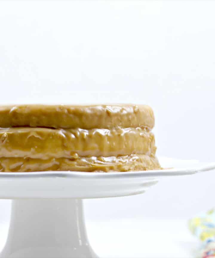 Side of a whole caramel cake on a white cake stand. 