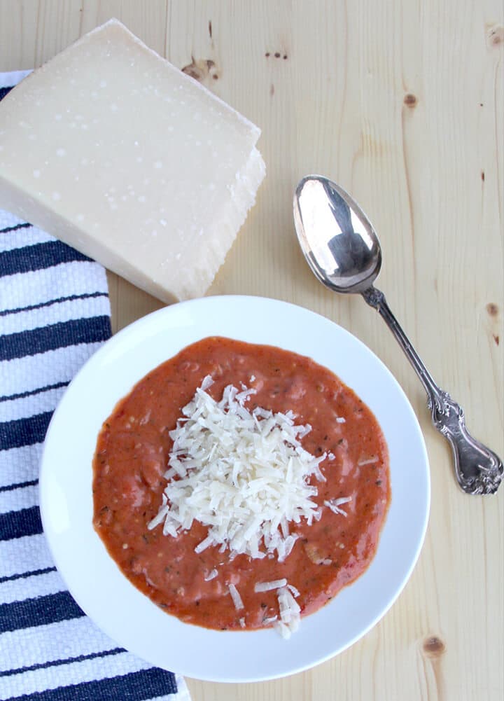 Overhead photo of a bowl of tomato soup with a block of parmesan cheese.