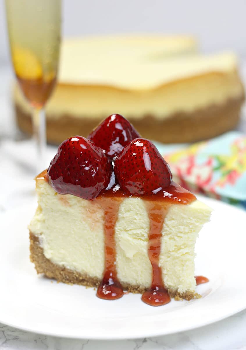 Side view of a slice of new york-style cheesecake with strawberries on top.