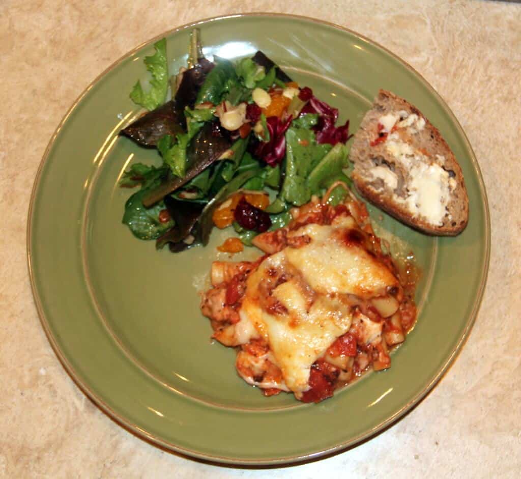 a plate with baked ziti, bread, and salad