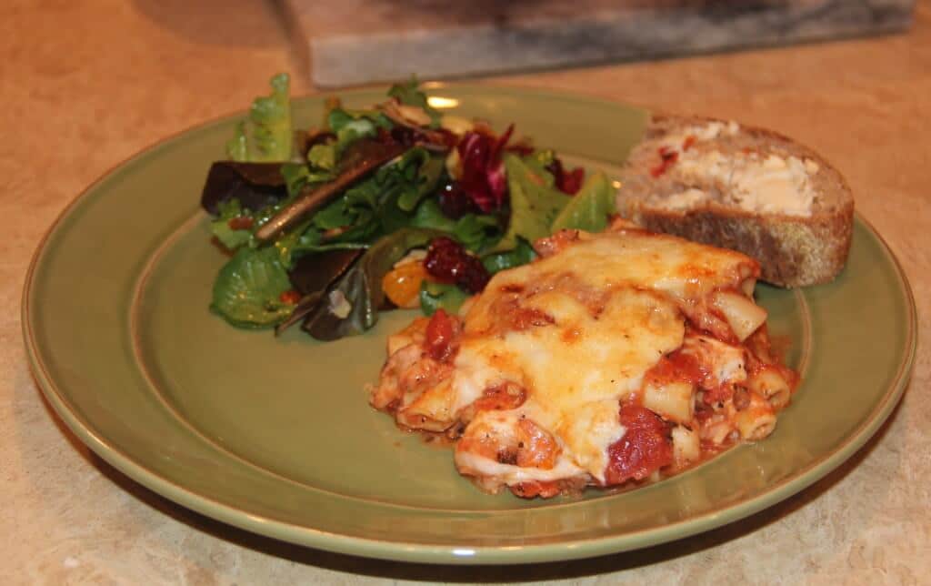 a green plate with baked ziti and salad