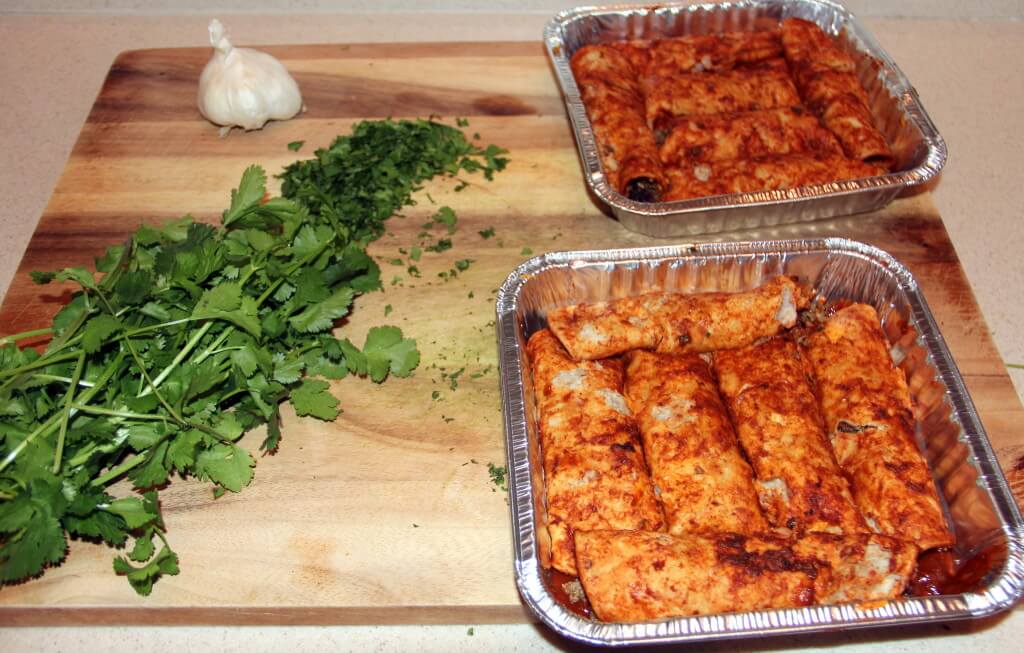 Two pans of beef enchiladas with cilantro on a cutting board.