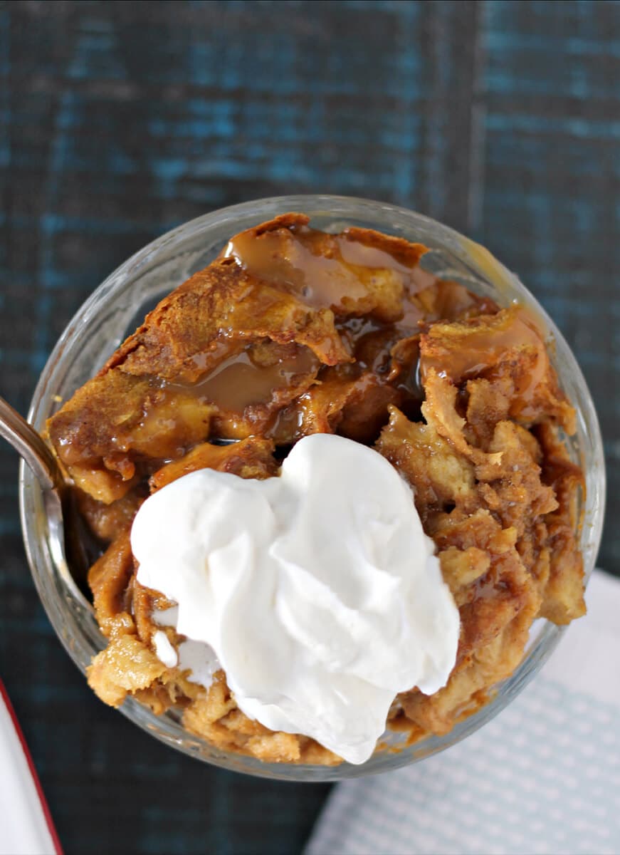 Overhead shot of a serving of pumpkin bread pudding in a dish with whipped cream.