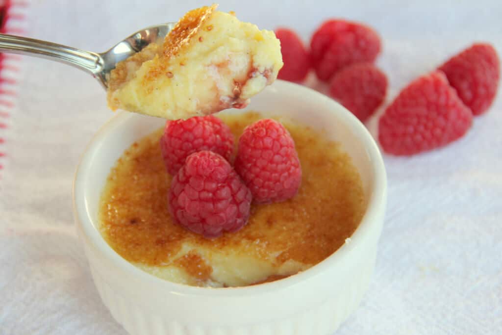 A spoonful of creamy white chocolate creme brulee with raspberries in background.