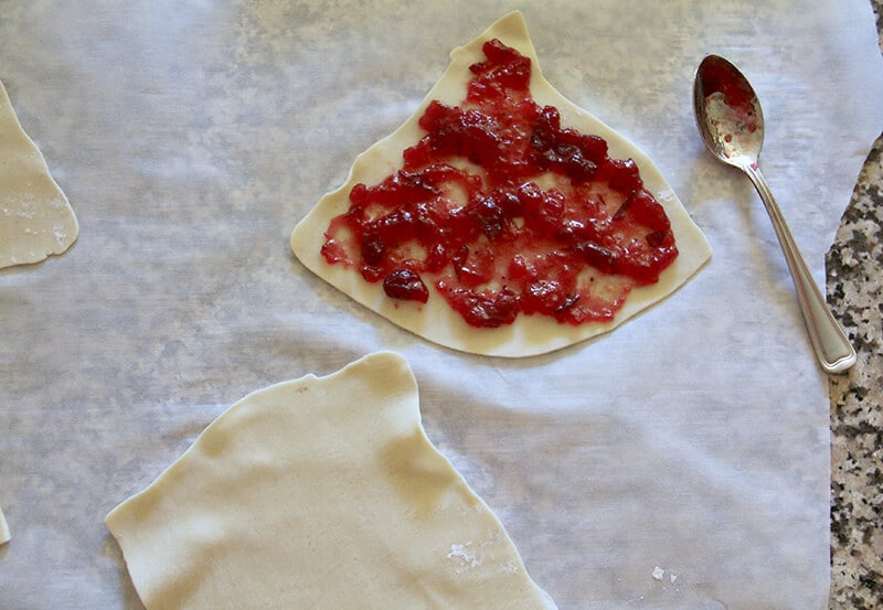 Overhead shot of cranberry sauce on pie dough with a spoon beside it. 
