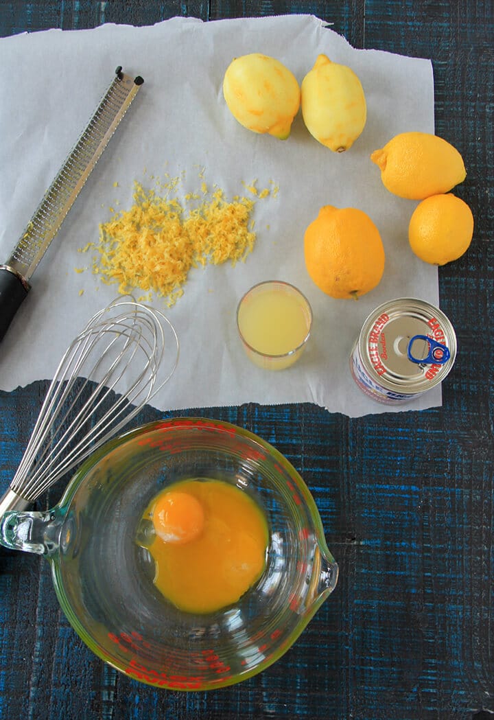 A bowl with egg yolks and a whisk, with lemons and zest for lemon icebox pie.
