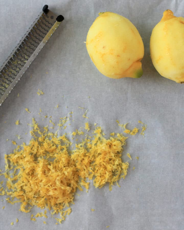 Two lemons with zest and a grater on parchment paper for making lemon icebox pie.