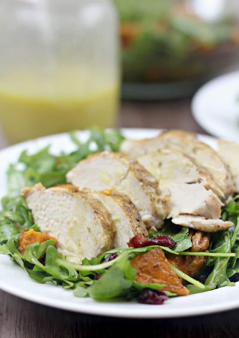 Arugula salad with roasted sweet potatoes, chicken, and honey-roasted pecans in bowl.