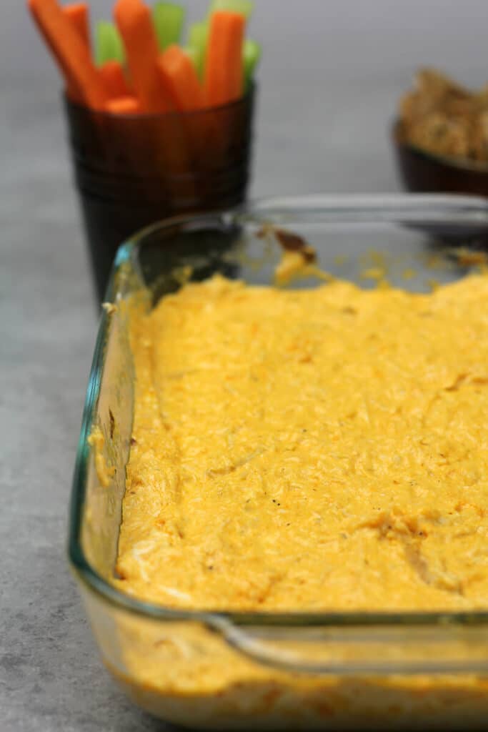 Side view of dish of Easy Buffalo Chicken Dip with jar of celery and carrots in the background.