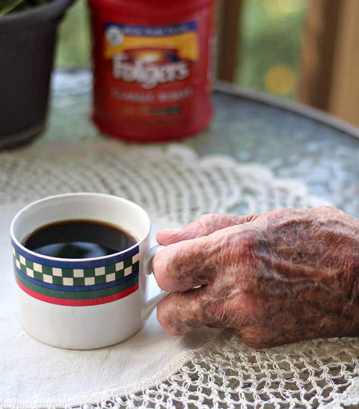 Elderly man's hand holding a cup of coffee on a table.