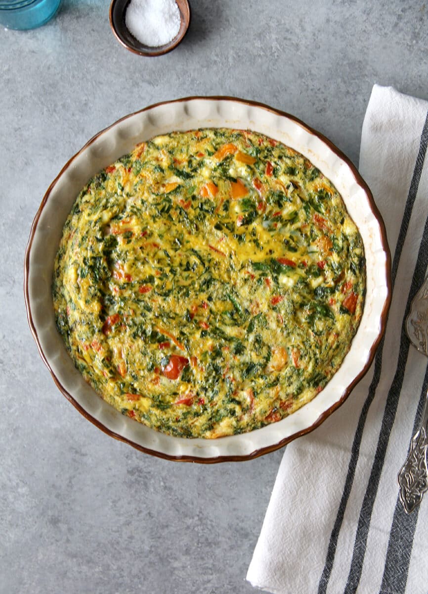 Overhead photo of the easy crustless quiche in a pie plate with a towel and bowl of salt. 