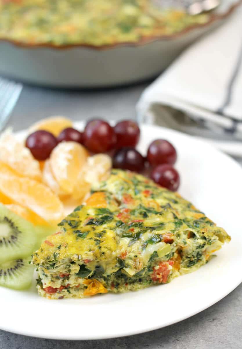 Slice of easy crustless quiche on a plate with grapes and tangerines. 