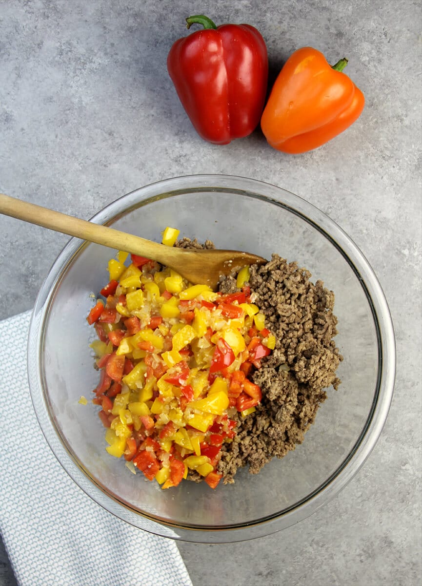 A clear glass bowl filled with cooked ground beef and chopped peppers for unstuffed pepper casserole. 