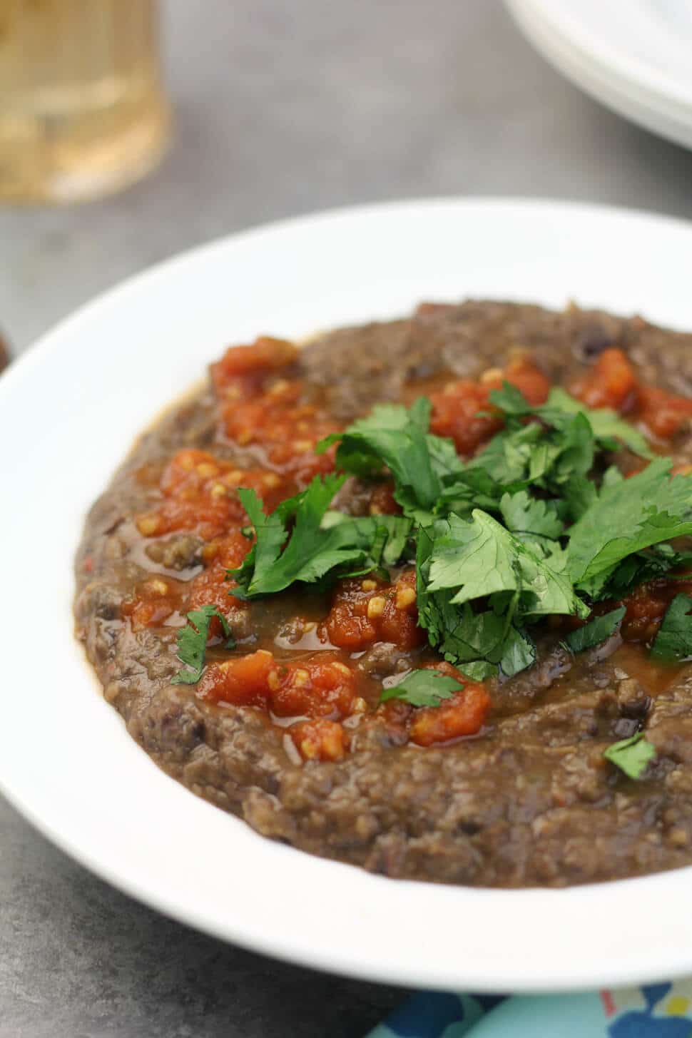 Close up photo of a white bowl filled with easy black bean soup garnished with cilantro and salsa. 