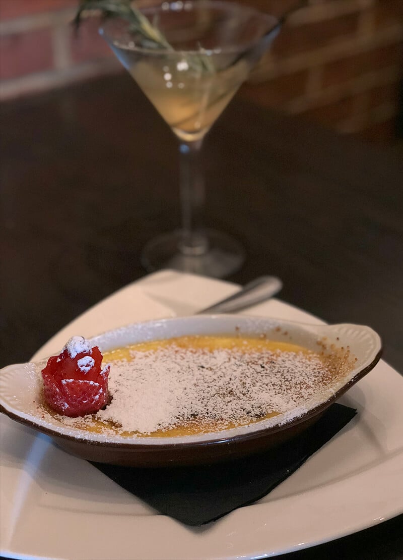 A dish of creme brulee from the Local Goat with a cocktail glass in the background.