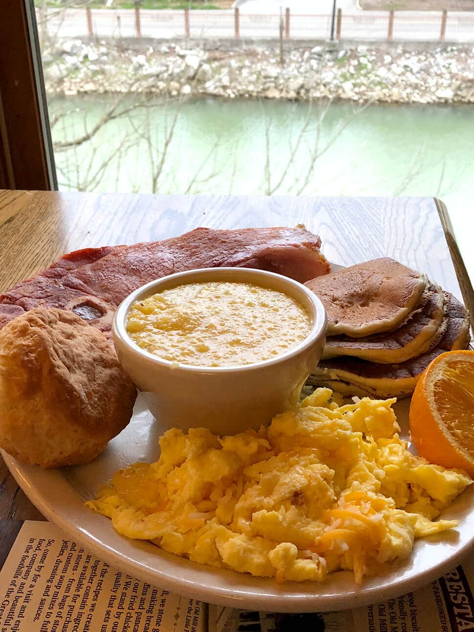 A plate of eggs, grits, and ham on a table that looks out to the river in Pigeon Forge at the Old Mill Restaurant.