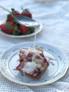 Strawberry Bars on a plate with a spoon drizzling lemon glaze.