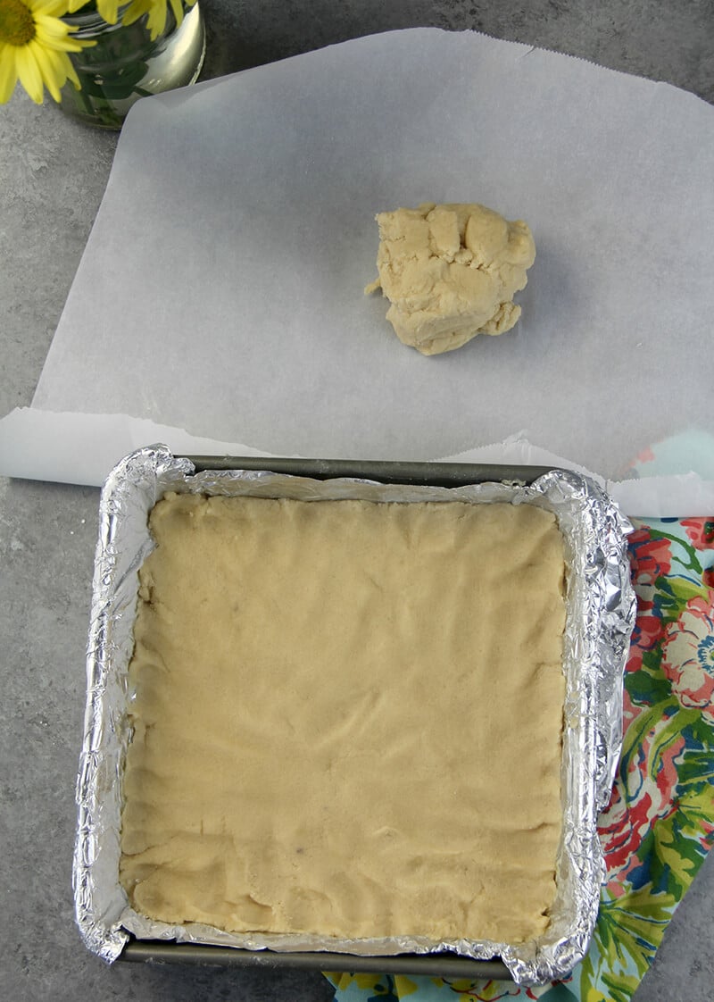 Baking pan with shortbread dough and extra dough on parchment paper on the side.