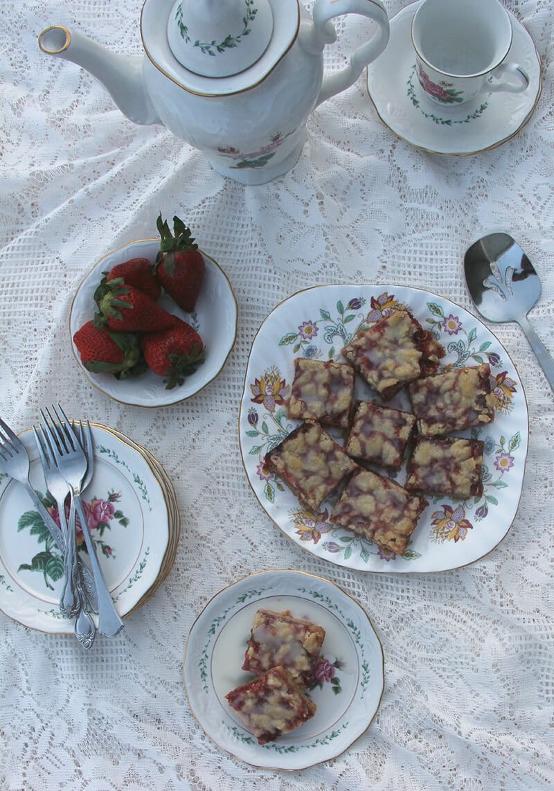Overhead shot of strawberry bars on a platter with a tea pitcher and cup and saucer.