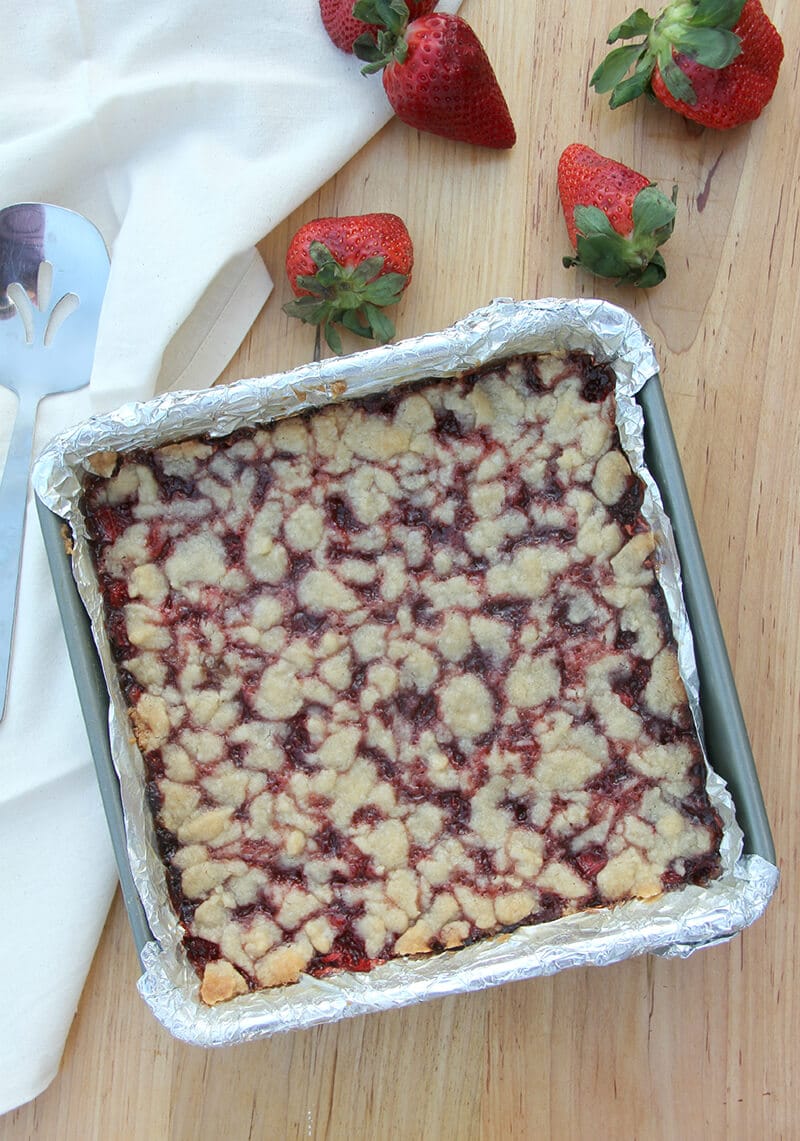 Baked strawberry bars in a baking pan with strawberries on the side.