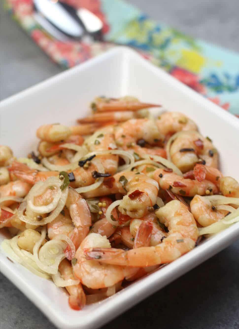 Pickled shrimp in a white bowl with spoon and colored napkin in the background. 