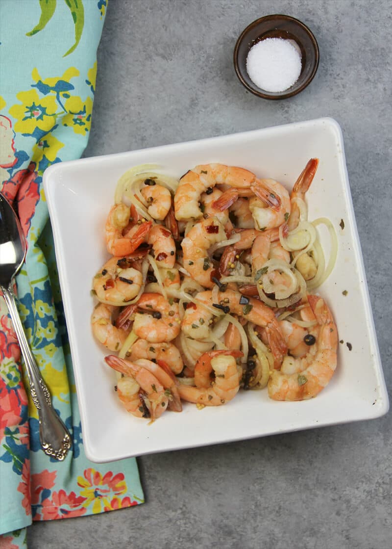 Overhead view of pickled shrimp in a white bowl with a small bowl of salt. 