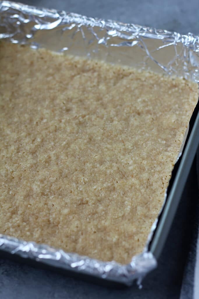The shortbread crust cooling in a foil-lined pan for white chocolate cheesecake bars.