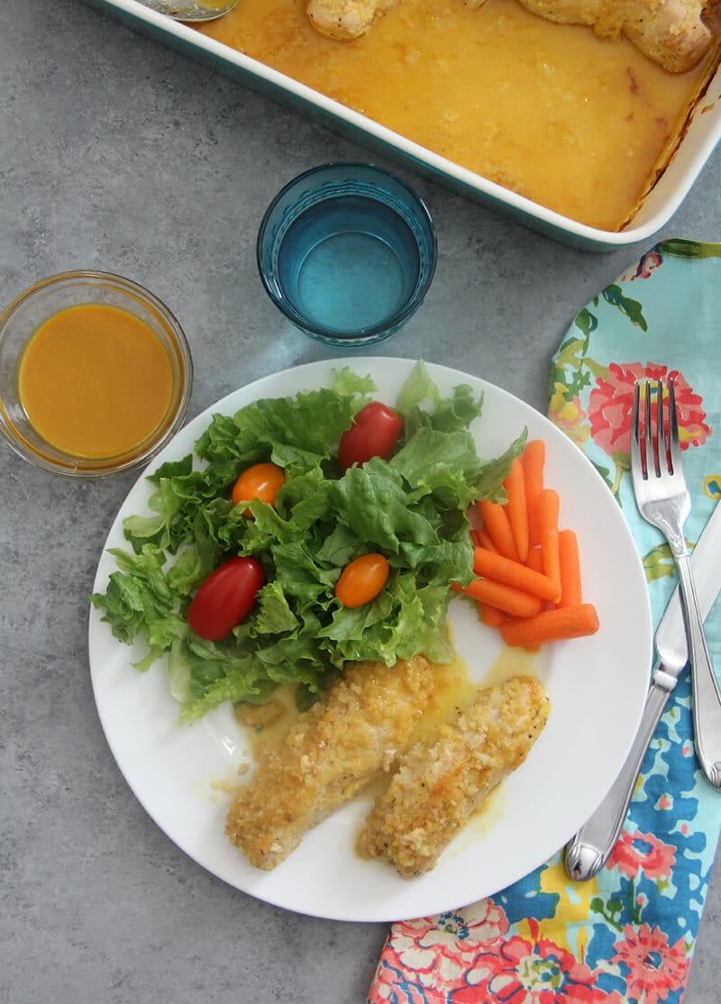 A plate of chicken and salad with a serving of honey mustard.