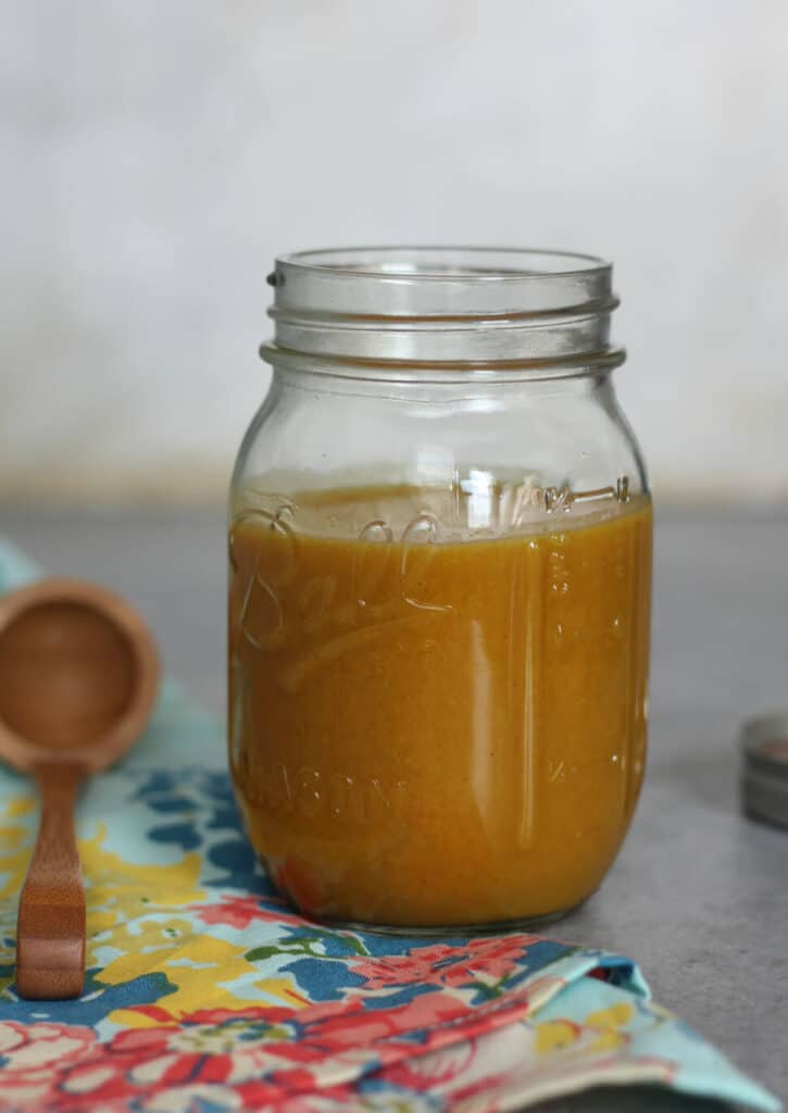 A jar of honey mustard sauce next to a wooden spoon.