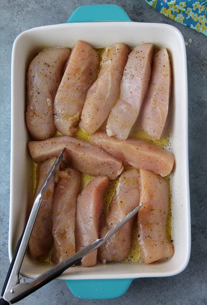 Cut up chicken pieces covered with olive oil and placed in a dish with tongs. 