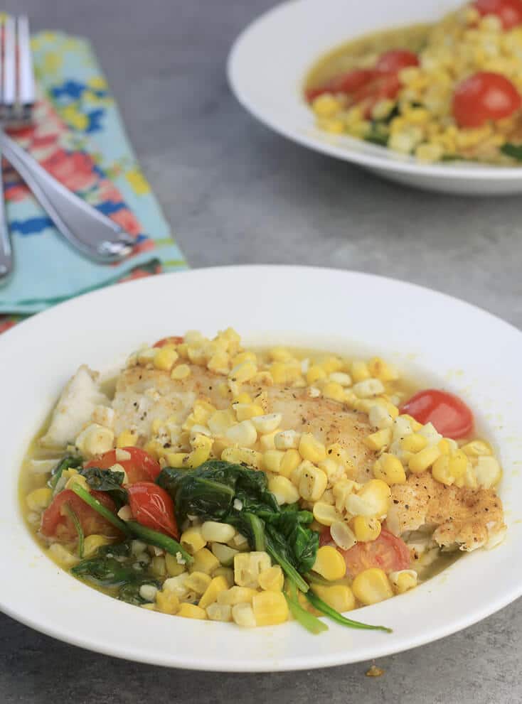 Oven baked fish in a bowl with corn and tomatoes.