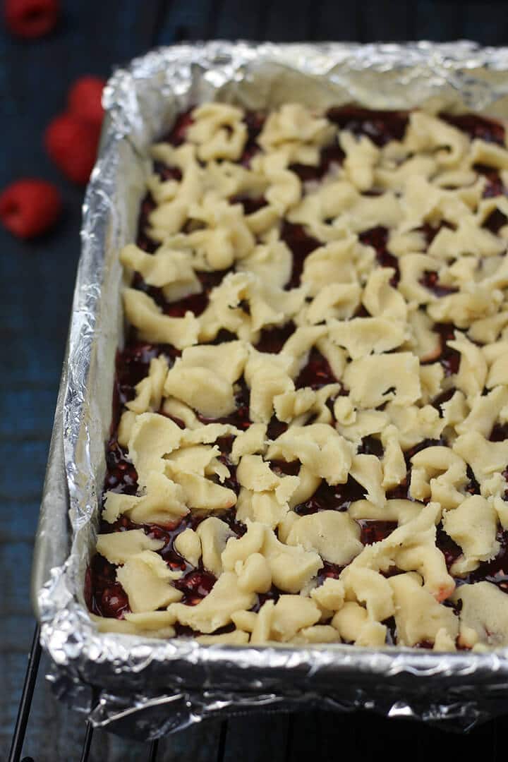 Crumbled shortbread on top of raspberry filling in the pan.