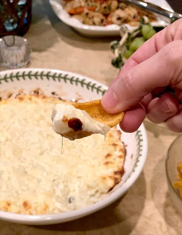 A bowl of onion dip with a hand holding a chip.