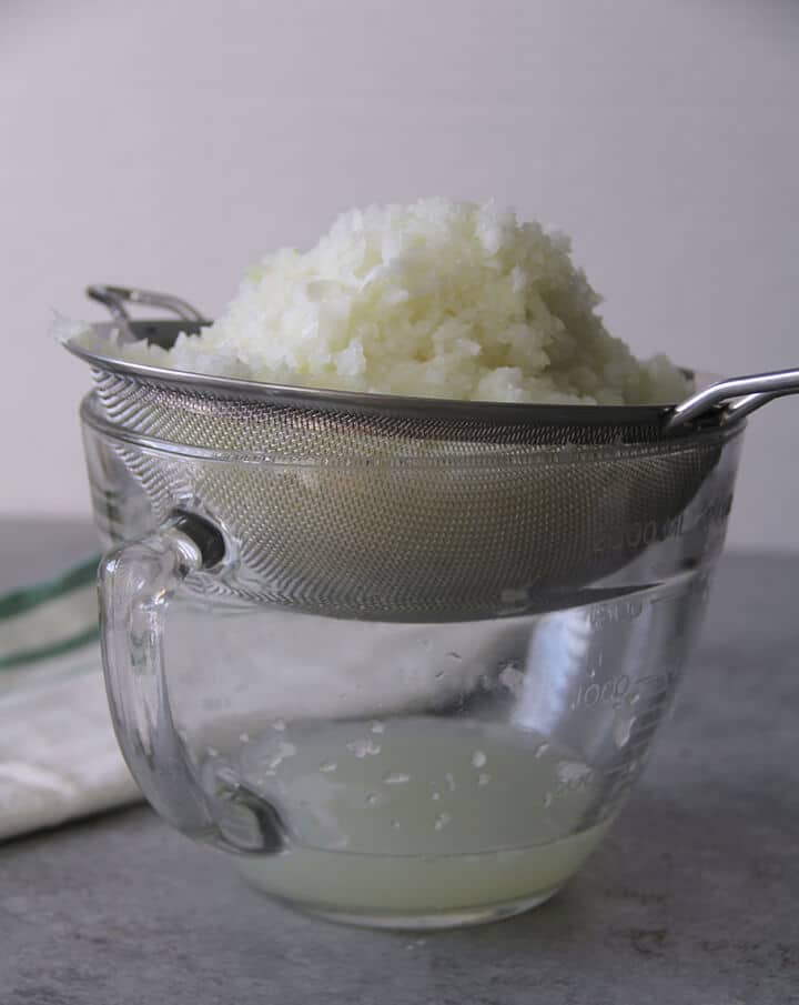 A mesh strained filled with chopped onions draining into a bowl.