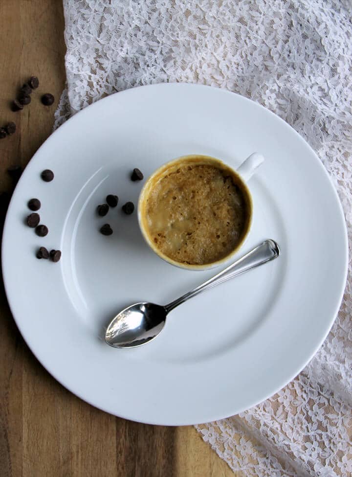 Overhead photo of a full cookie in a mug with a spoon on a white plate.